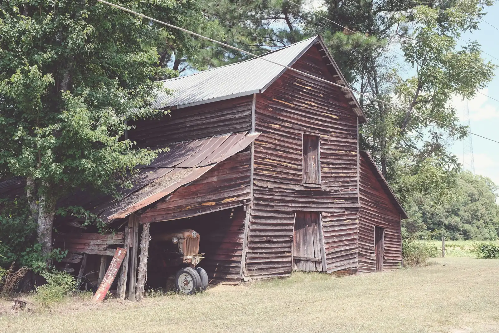 Weathered wooden barn with an old tractor under tall trees in Pelzer, Anderson County, South Carolina