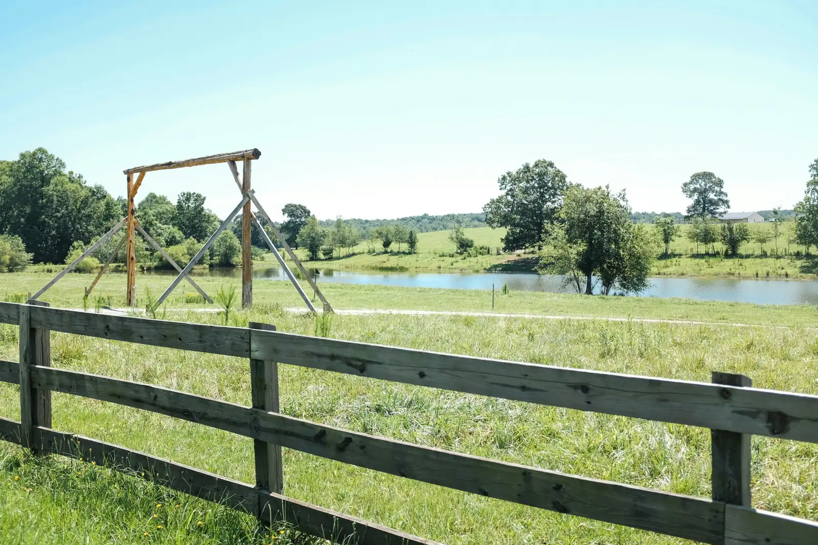 Wooden fence, green pasture and a farm pond on a sunny day in Tigerville, northern Greenville County, South Carolina